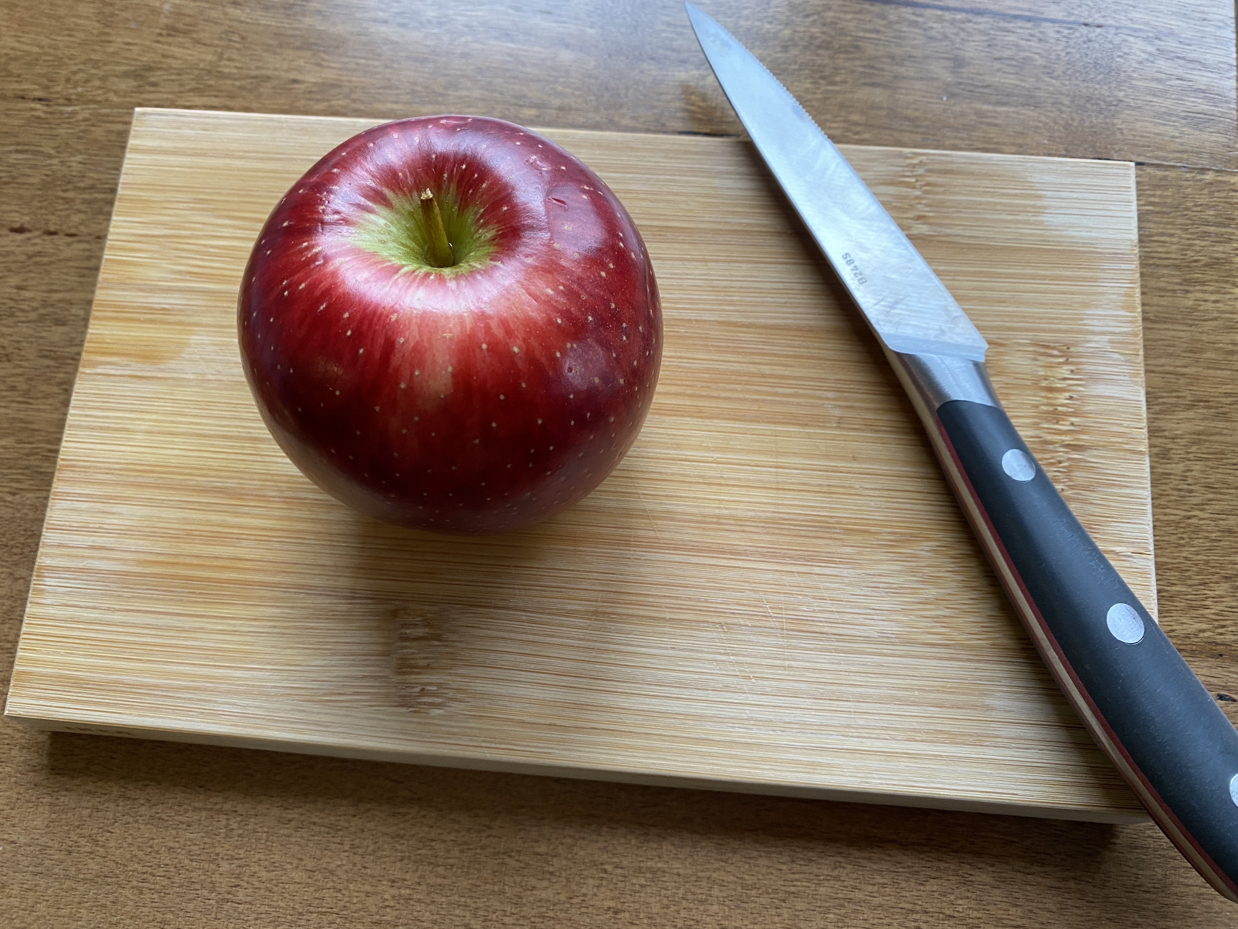Whole apple and knife on cutting board.