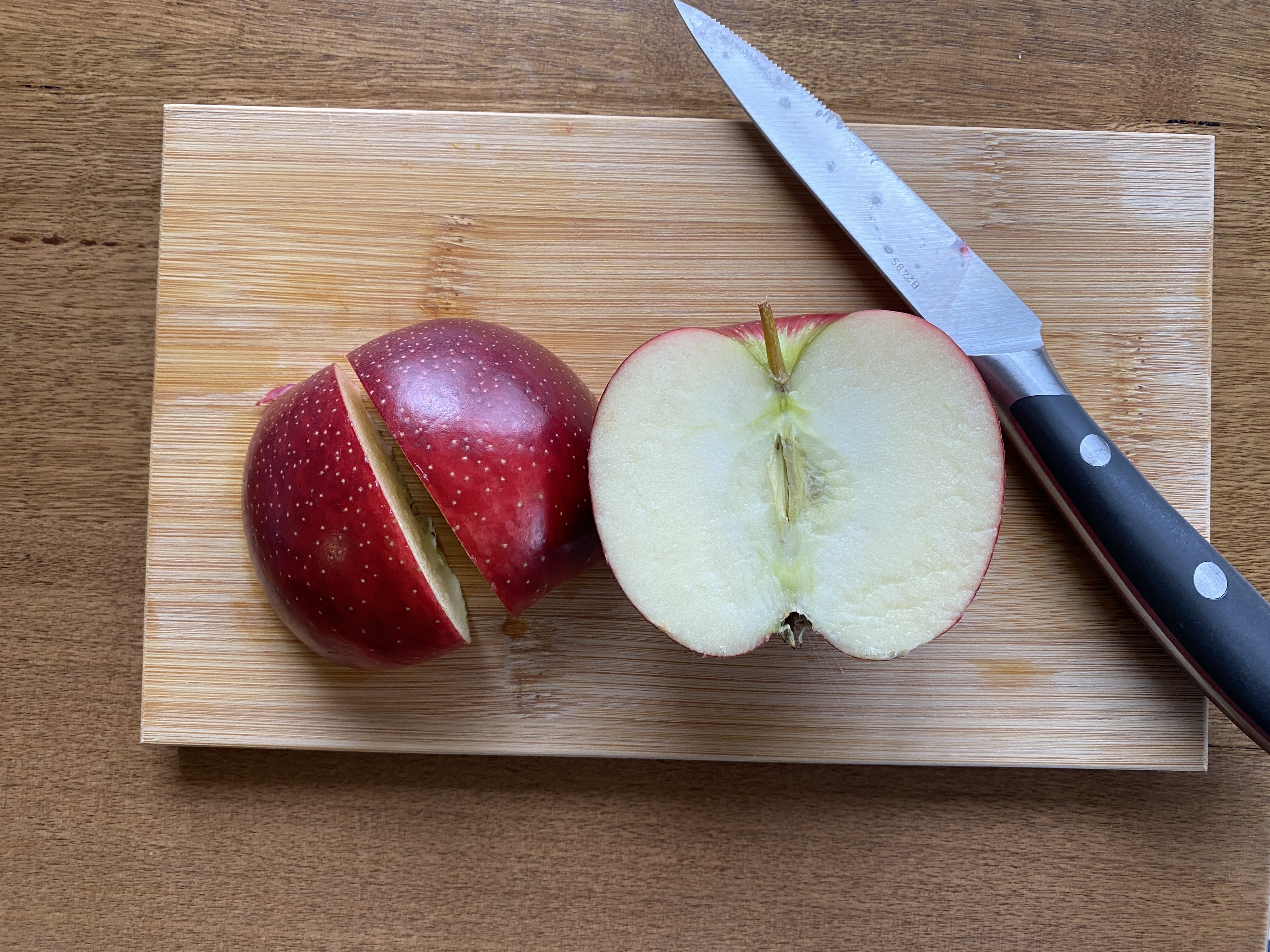 Apple in two halves and knife on cutting board.