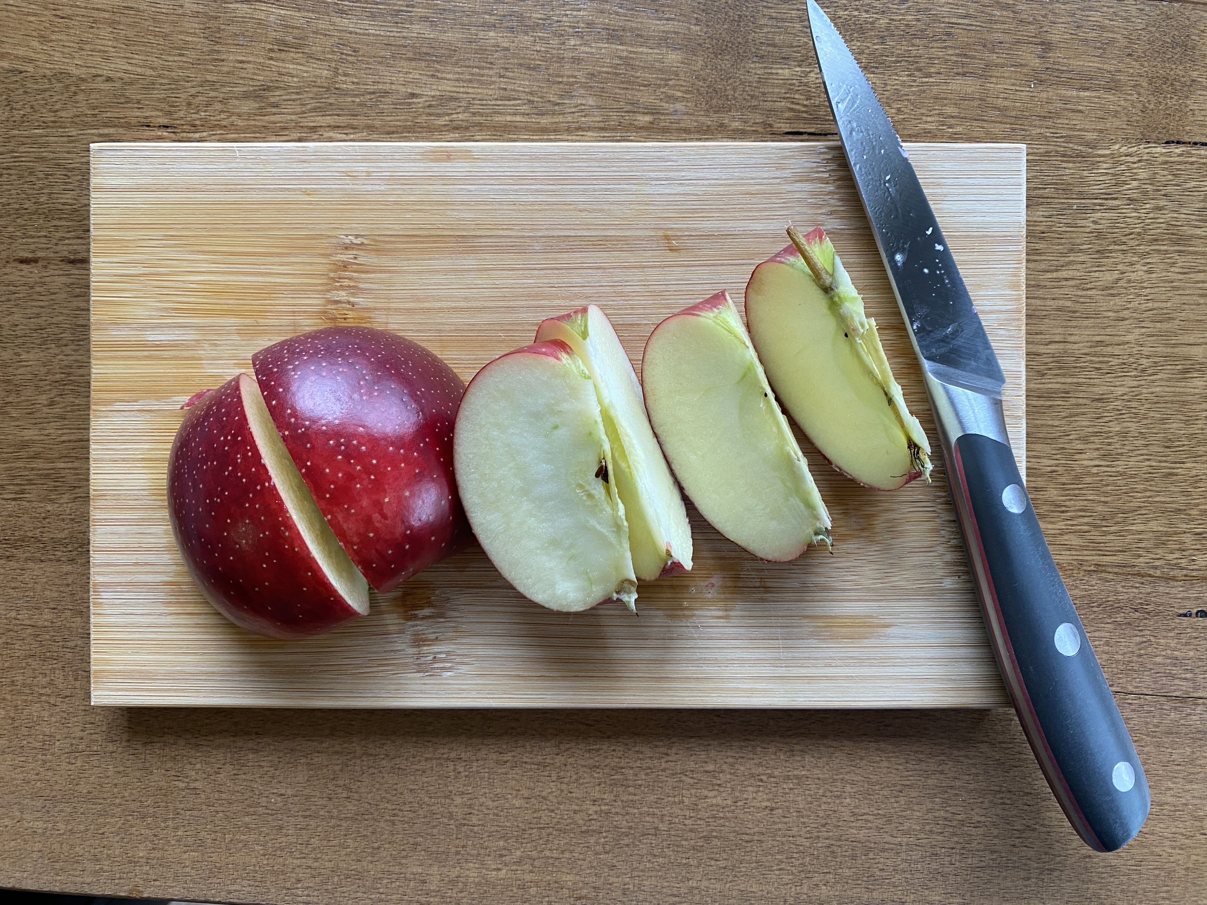Apple sliced into eighths and knife on cutting board.