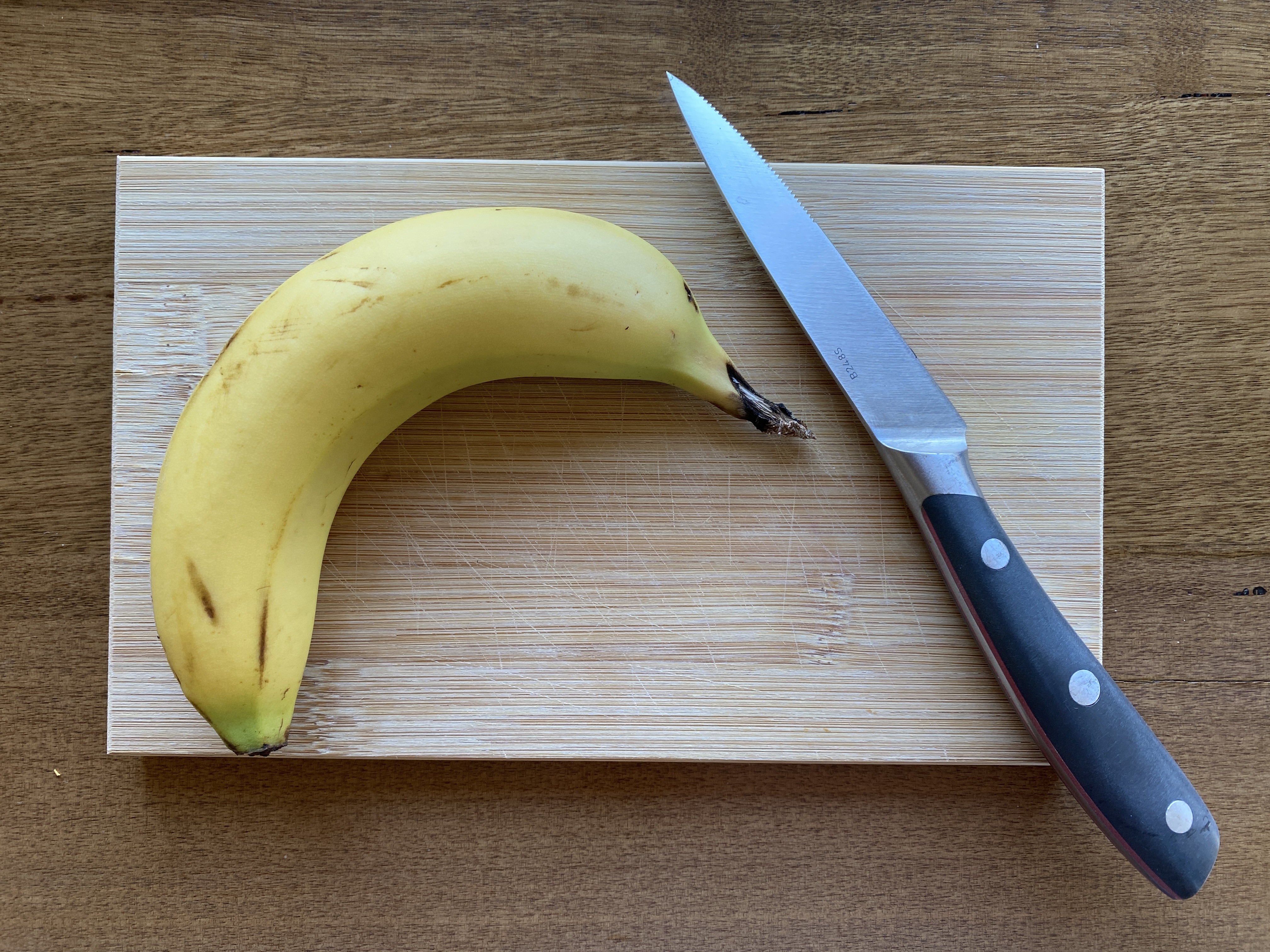 Whole banana and knife on cutting board.