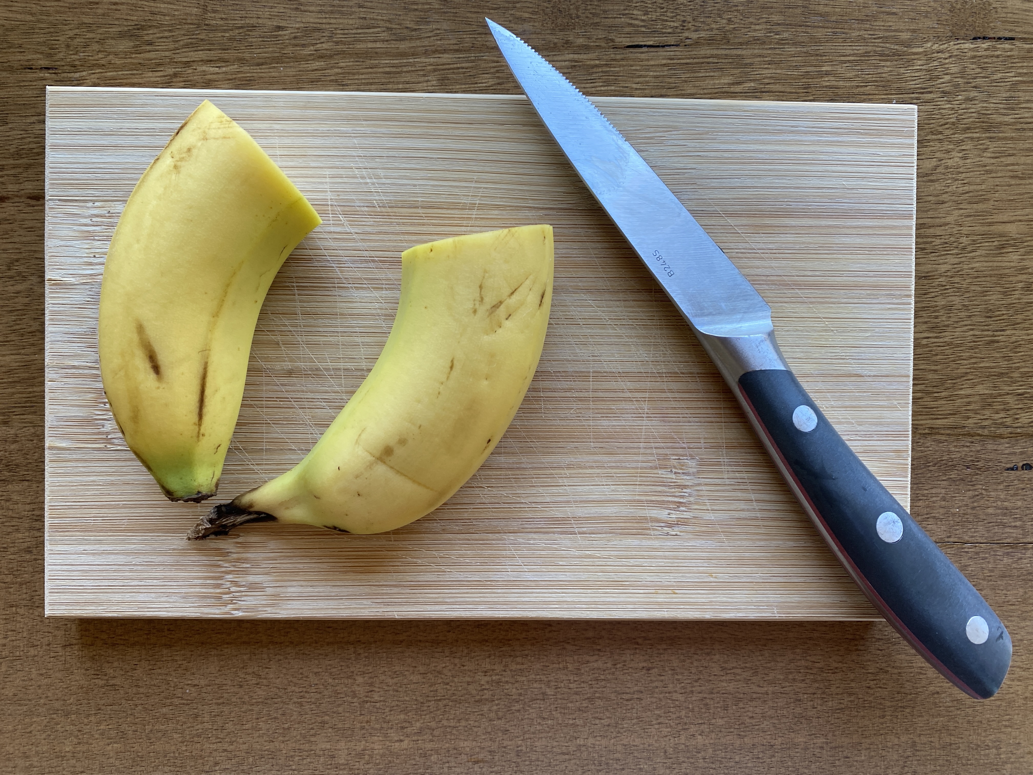 Banana in half and knife on cutting board.