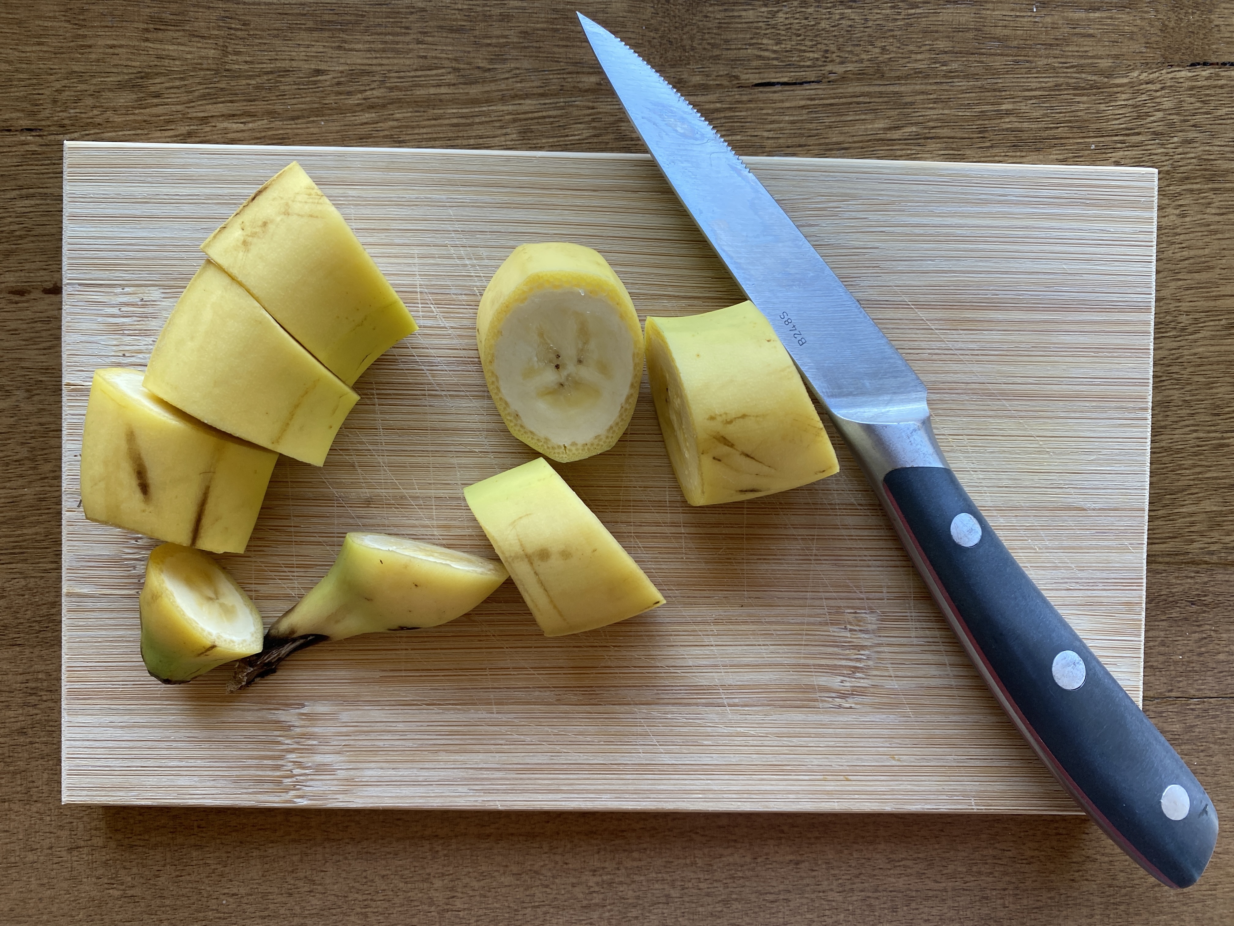 Banana cut into eight coin-shaped pieces and knife on cutting board.